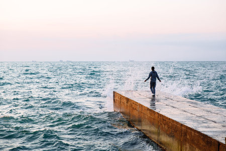 Full length view of young man in sportswear jumping with skipping rope, workout on pier, near the...