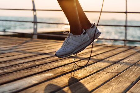 Close-up photo of jumping male, legs in flight with skipping rope, workout on quay, near the sea. Healthcare.の写真素材
