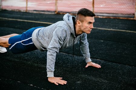 Portrait of a fit handsome sportsman doing plank exercise, practicing pushs up on track road, dressed in sportswear, outdoorsの写真素材