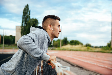 Profile view of attractive young guy doing exercises, push-ups, workout, listening to music,...