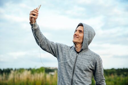 Profile view of active handsome runner taking a selfie with smartphone, listening to music, outdoorsの写真素材