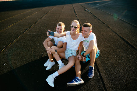 Selfie of three friends while girl is sitting on a penny skateboard.