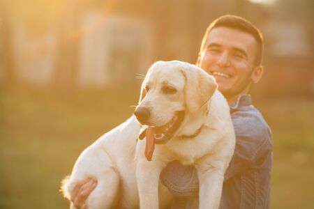 Happy man holding his dog labrador in hands in park at sunset. Toned photoの写真素材