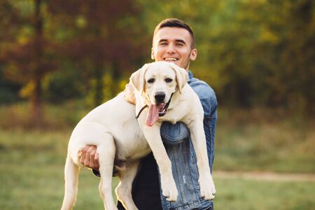 Portrait of happy man holding dog Labrador in hands in parkの写真素材