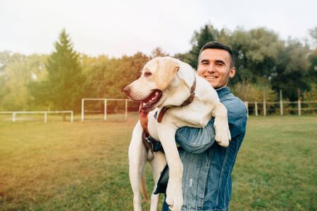 Smiling man holding his dog Labrador in hands in parkの写真素材