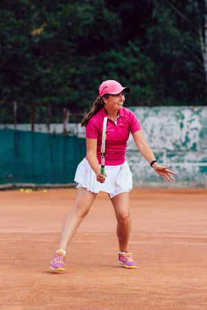 Tennis player. Full length photo of beautiful young woman playing tennis, waiting to receive serve. Dressed in colorful sportswear.の写真素材