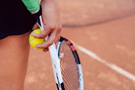 Woman holding tennis racket and ball on clay court. Close-up. Sport concept.の写真素材