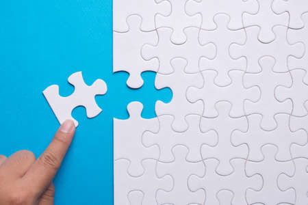 Hand holding piece of white puzzle on blue background. Business and team work concept.の写真素材