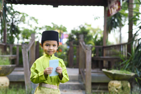 A Malay boy in Malay traditional cloth showing his happy reaction after received money pocket during Eid Fitri or Hari Raya celebration.の写真素材