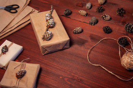 Handmade craft paper box on a wooden surface, decorated with a branch with fir cones. Nearby packing...