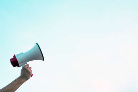 Arm entering in the image and a hand holds a megaphone with a space to dispose of the according interest.の写真素材