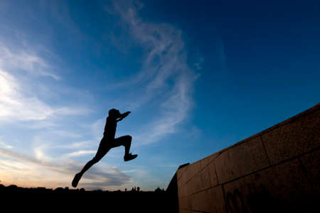 Young man practicing parkour in the street with a blue sky and backlightの写真素材