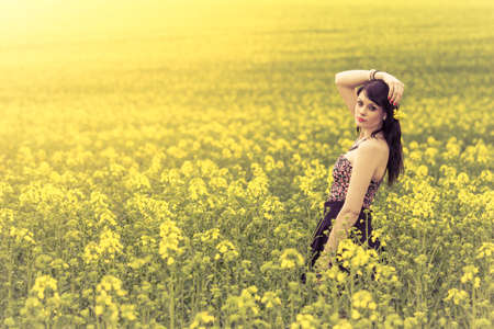 Beautiful woman in meadow of yellow flowers with arm up. Attractive genuine young girl enjoying the warm summer sun in a wide green and yellow meadow. Part of series.の写真素材