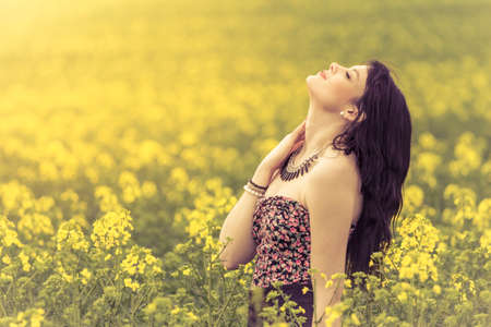 Beautiful woman in meadow of yellow flowers with face up. Attractive genuine young girl enjoying the warm summer sun in a wide green and yellow meadow. Part of series.の写真素材