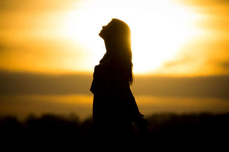 Twilight silhouette by beautiful sunny young woman in summer. The sun stands at the horizon and the girl Becomes a very nice black silhouette.の写真素材