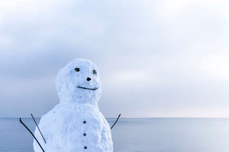 Snowman in beautiful white winter wonderland lake at xmas time. Traditional man of snow at a cool and snowy sea scene.の写真素材