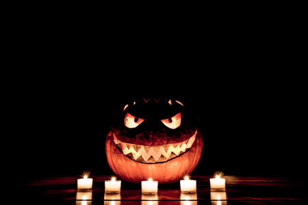 Candlelight halloween pumpkin smile with burning fire eyes mouth. Big spooky helloween symbol has a glowing mad face and smiling with sharp teeth and bad look. Black orange nightmare of October 31st.の写真素材