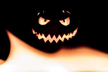 Fire flames halloween pumpkin smile with hot burning eyes mouth. Big spooky helloween symbol has a glowing mad face and smiling with sharp teeth and bad look. Black orange nightmare of October 31st.の写真素材