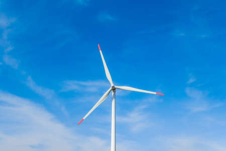 Rotating windmill generating renewable energy with wind power. Sustainability by windmills turbines preventing climate change with regenerative clean green nature energy. Windy blue sky with cloudsの写真素材