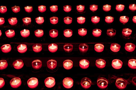 Group of red candles in church for faith resurrection prayer. Candlelight fire flames in rows are silent religion symbol for peace, life and soul. Obituary hope sacrifice against sorrows and pain.の写真素材