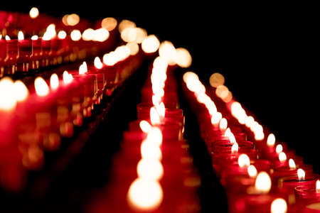 Group of red candles in church for faith resurrection prayer. Candlelight fire flames in rows are silent religion symbol for peace, life and soul. Obituary hope sacrifice against sorrows and pain.の写真素材