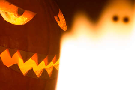 Spooky carved halloween pumpkin and creepy mystery fire ghost. Big helloween autumn symbol with mad face, glowing eyes, mouth and teeth. Scary hot nightmare horror with evil smile at october 31st.の写真素材