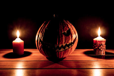 Carved spooky halloween pumpkin two burning candle fire flames. Big helloween autumn symbol with mad face, glowing eyes, mouth and teeth. Scary hot nightmare horror with evil smile at october 31st.の写真素材