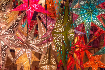 Group colorful seasonal xmas lantern stars at christmas market. Traditional shopping decoration at x-mas markets in holiday advent. Bright shiny glowing colors for best miracle time of the year.の写真素材