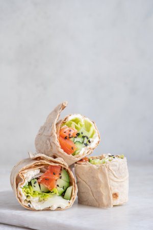 Tortilla with salmon, creamy cheese and vegetables on white plateの写真素材