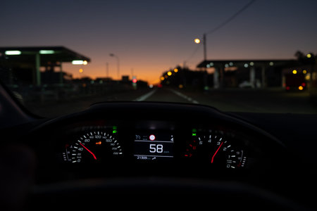 Driver view to the speedometer at 58 km/h or 58 mph, on a road with lights and station services on...
