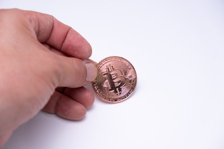 Male hand finger holding on table bitcoin cryptocurrency coin. close up to rose gold bit coin standing on white background. BTC most popular crypto currency money.の写真素材