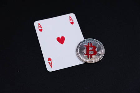 One Silver Bitcoin with logo on red colour, lied on top red ace card playing card on the desk with dark background.の写真素材