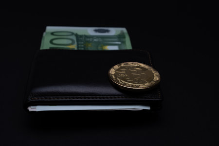 Bitcoin coin on top of wallet with  100 Euros banknotes on a dark background. Golden bitcoin on wallet one hundred euro bank notes. Cryptocurrency concept and Euros banknotes.の写真素材