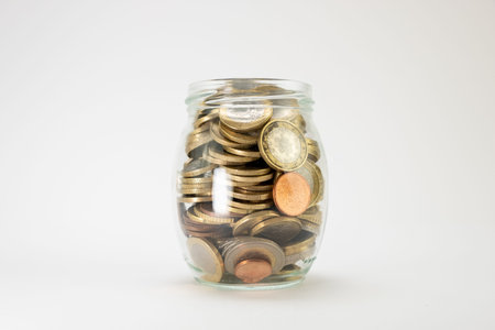 Glass jar full until the top with euro coins, centered on a white background, side view. Euro coins...