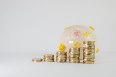Stacked euro coins with piggy bank behind, on a white background. Concept of saving money. copy...