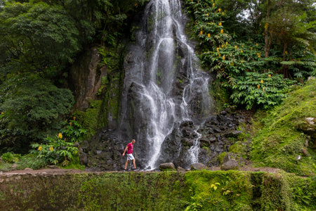 Nordeste, Azores - 07.09.2019: Tourist walking in front of a Waterfall in the Botanical Garden of Ribeira do Guilherme in Nordeste, Sao Miguel island in the Azores.のeditorial素材
