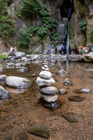 A group of zen stones in a stream surrounded by tourists. With the Waterfall of Salto do Cabrito in...