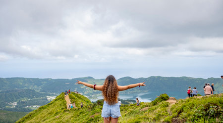 Young woman with curly hair with arms outstretched, standing on top of the mountain looking to Sete Cidades Lake, from near the Grota do Inferno. Sao Miguel, Azoresの写真素材