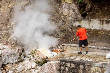 Furnas, Azores - 06.08.2023: Man removing sweet corn cobs cooked on the geyser hot springs on sacks. A typical snack from Furnas in the island of Sao Miguel, Azores in Portugalのeditorial素材