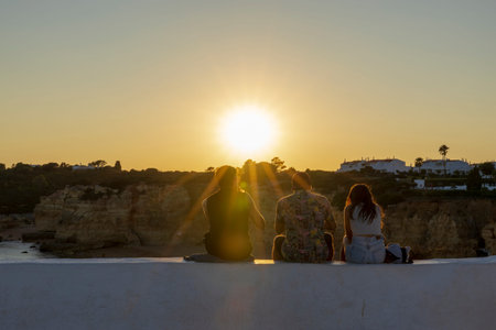 Young friends sitting on the wall, enjoying the sunset on a beach of Algarve, Portugal.の写真素材