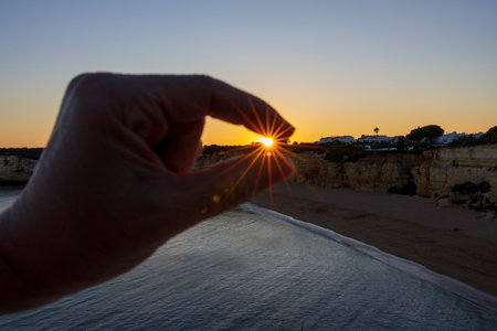 Hand catching the sun on a sunset on a beach of the Algarve, Portugal.の写真素材