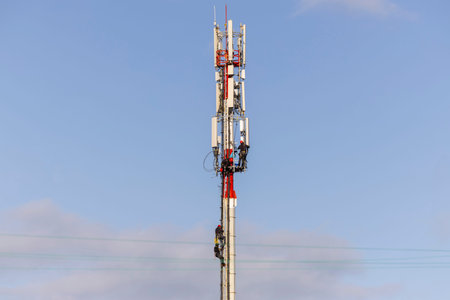 Technicians assembling antennas for 5G cellular communication on a telecommunications tower. Base...