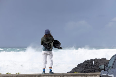 Young woman looking at the ocean waves on a stormy day. Sao Miguel island, Azores, Portugal.