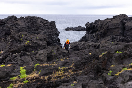 Man wearing Coasteering suit walking along the black volcanic cliffs on the island of Sao Miguel in...