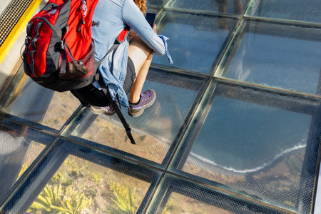 Tourist standing on the transparent glass skywalk of the viewpoint of Cabo Girão. Madeira island, Portugal.の写真素材