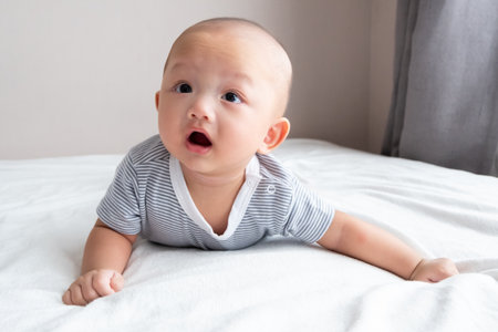 baby boy with big eyes smiling with mouth open on the white mattress
