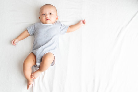 Top view and side areaA baby wearing a striped shirt, spreading arms and legs on a white carpet.