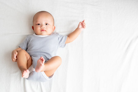 top view
A baby wearing a striped shirt, raising his arms and legs on a white carpet.の写真素材