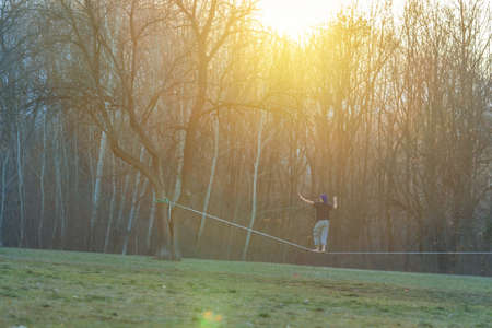 Handsome young man walking on slackline in the park at sunsetの写真素材