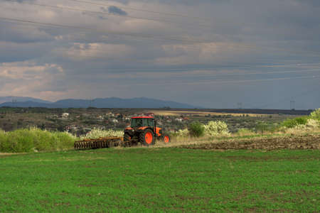 Farmer with tractor seeding crops at field in springの写真素材